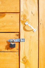 a small metal padlock hangs on the closed wooden door of the house, a shed made of wooden boards with large slits. background, backdrop in the form of a closed door with a structure of wood, lumber