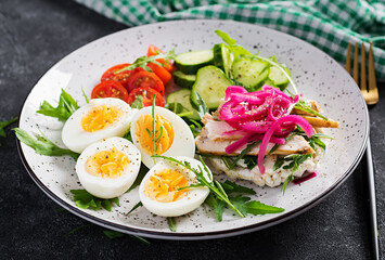 Breakfast. Boiled eggs salad with greens, cucumbers, tomato and sandwich with ricotta cheese, fried chicken fillet and red onion. Keto/paleo lunch.