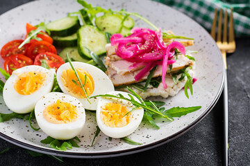 Breakfast. Boiled eggs salad with greens, cucumbers, tomato and sandwich with ricotta cheese, fried chicken fillet and red onion. Keto/paleo lunch.