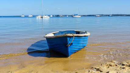 View past blue row boat on the beach to boats moored on the calm blue sea 