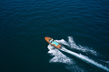 Fototapeta premium Top view of a wooden open large motor boat. Luxurious wooden boat fast movement on dark water. Classic Italian wooden boat fast moving aerial view.