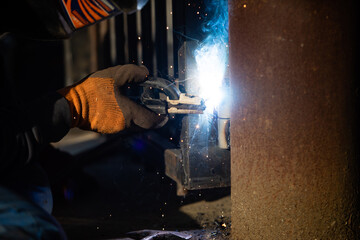 The man in uniform welds a metal at the factory