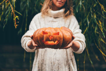 Woman shows spooky carved Jack-O-Lantern face made of large orange pumpkin celebrating Halloween...