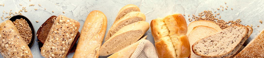 Various types of fresh baked bread on light gray background.