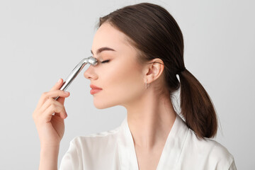 Beautiful young woman with facial massage tool on light background