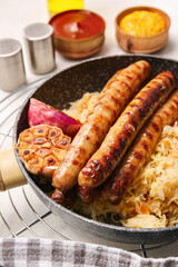 Frying pan with tasty sauerkraut and grilled sausages on light background, closeup