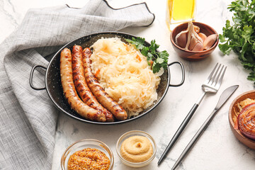 Frying pan with tasty sauerkraut, grilled sausages and sauces on light background