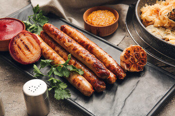 Board with tasty grilled sausages and sauces on grunge background, closeup