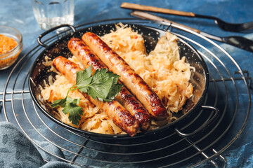 Frying pan with tasty grilled sausages and sauerkraut on color background