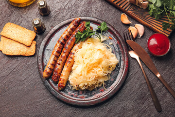 Plate with tasty grilled sausages and sauerkraut on dark background