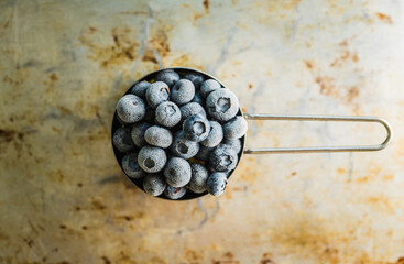 Frozen blueberries in metal cup on the rustic background. Selective focus.