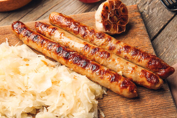 Board with tasty sauerkraut and grilled sausages on wooden background, closeup