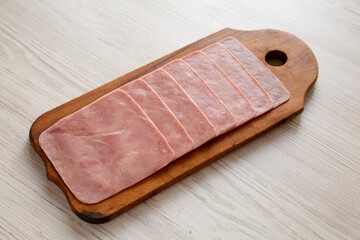 Organic Jamon Cocido Extra on a rustic wooden board on a white wooden surface, side view.