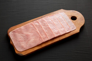 Organic Jamon Cocido Extra on a rustic wooden board on a black surface, side view.