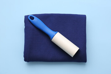 Lint roller and clothes on color background