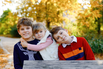 Fototapeta premium Portrait of three siblings children. Two kids brothers boys and little cute toddler sister girl having fun together in autumn park. Happy healthy family playing, walking, active leisure on nature