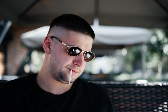 cloae up view of  young black haired man witn sunglasses smoking tabacco  in outdoor cafe