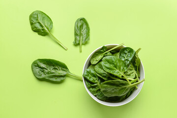 Bowl with fresh spinach leaves on color background