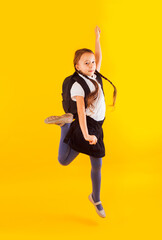 Jumping emotional schoolgirl on the yellow background