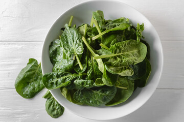 Bowl with fresh spinach leaves on light wooden background, closeup