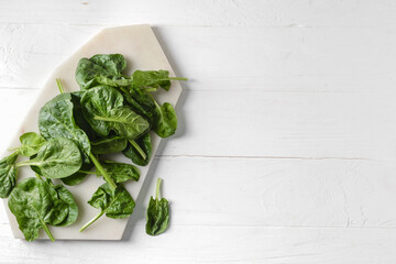 Board with fresh spinach leaves on light wooden background