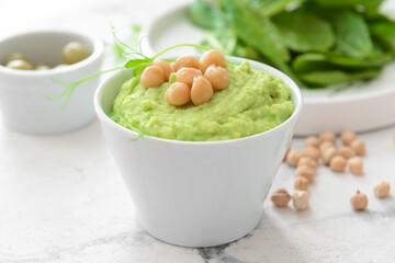 Bowl with tasty green pea hummus and chickpeas on light background, closeup