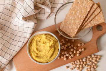 Bowl with tasty hummus, chickpeas and crackers on light background