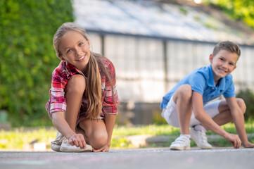 Girl and boy drawing with crayons in park