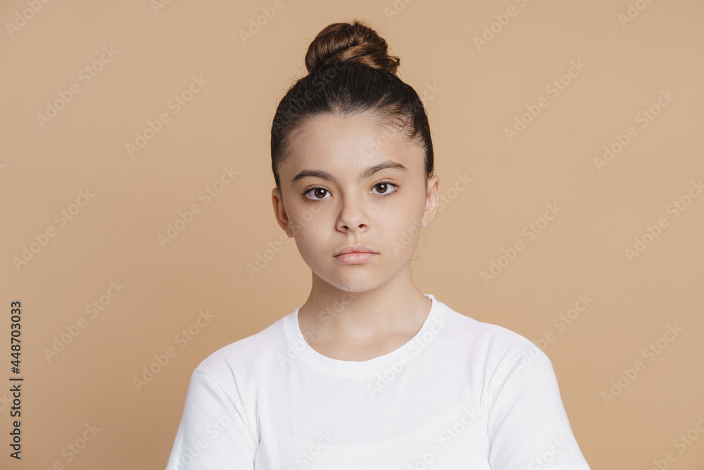 Wall mural Serious teenage girl with a bundle of hair looks at the camera. Cute little girl on a pink background