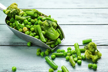 Scoop with frozen green vegetables on color wooden background