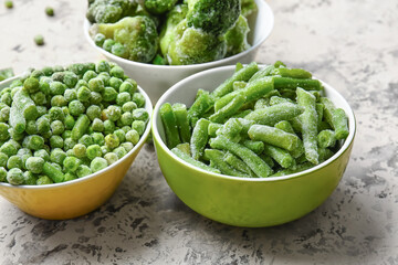 Bowls with frozen green vegetables on color background