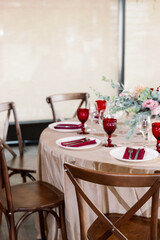 Decoration of the wedding table with red and pink flowers on a white tablecloth. Red glass goblets and burgundy napkins on the plates.