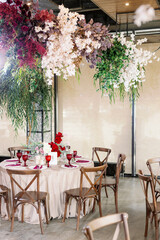 Decoration of the wedding table with red and pink flowers on a white tablecloth. Red glass goblets and burgundy napkins on the plates.