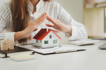 Female agent covering house model at table, closeup. Home insurance