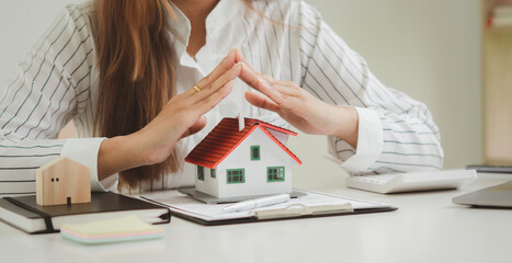 Female agent covering house model at table, closeup. Home insurance