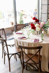 Indoor dinner party with served tables with red flowers and wooden vintage rustic boho chairs