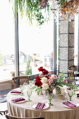 Indoor dinner party with served tables with red flowers and wooden vintage rustic boho chairs