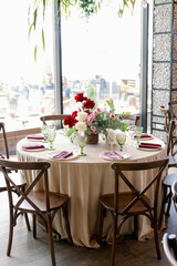 Decoration of the wedding table with red and pink flowers on a white tablecloth. Green glass goblets