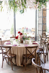 Indoor dinner party with served tables with red flowers and wooden vintage rustic boho chairs