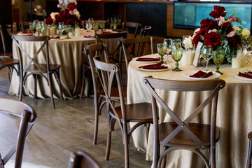 Fototapeta na wymiar Dinner party indoors with served tables in a restaurant with red flowers and wooden vintage chairs in rustic boho style