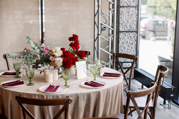 Decoration of the wedding table with red and pink flowers on a white tablecloth. Green glass goblets and framed table number.
