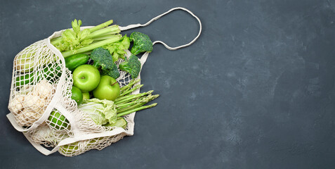 green vegetables and fruits in a reusable bag on dark concrete background
