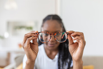 young African woman holds glasses with diopter lenses and looks through them, the problem of myopia, vision correction