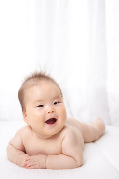 A naked, prone baby. Head raised in a smiling position.