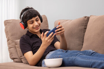 A HAPPY TEENAGER PLAYING VIDEO GAME ON MOBILE WHILE RESTING ON SOFA