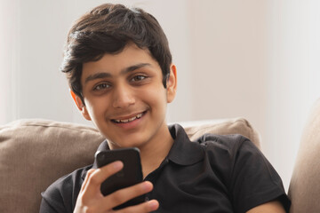 A TEENAGER HOLDING MOBILE PHONE HAPPILY LOOKING AT CAMERA