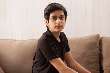 PORTRAIT OF A TEENAGE BOY SITTING AND LOOKING AT CAMERA
