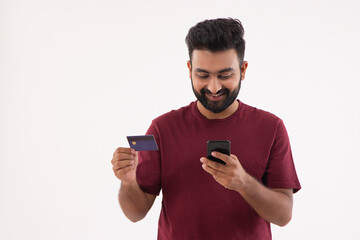 A CHEERFUL YOUNG MAN DOING ONLINE TRANSACTION USING DEBIT CARD AND MOBILE