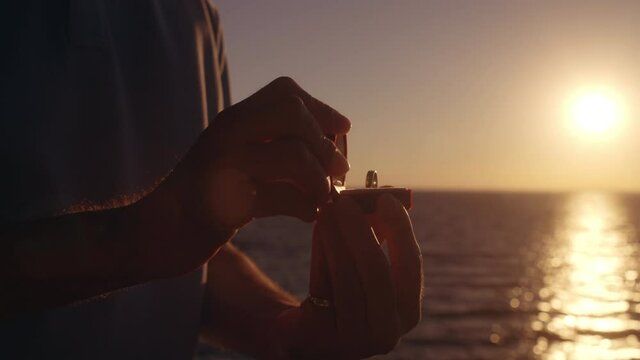 Male hands opening jewelry box with engagement ring, romantic proposal near sea