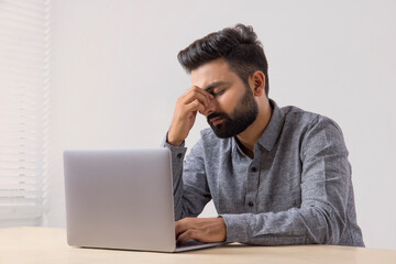 A BEARDED YOUNG MAN SITTING IN STRESS WHILE WORKING ON LAPTOP